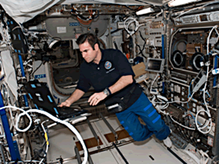 NASA astronaut Reid Wiseman working aboard the ISS among arrays of space-qualified cables and connectors.